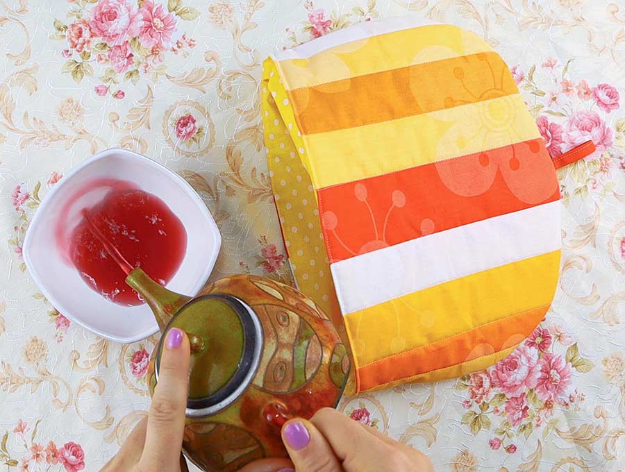 quilted teapot cozy and hands pouring tea from a kettle